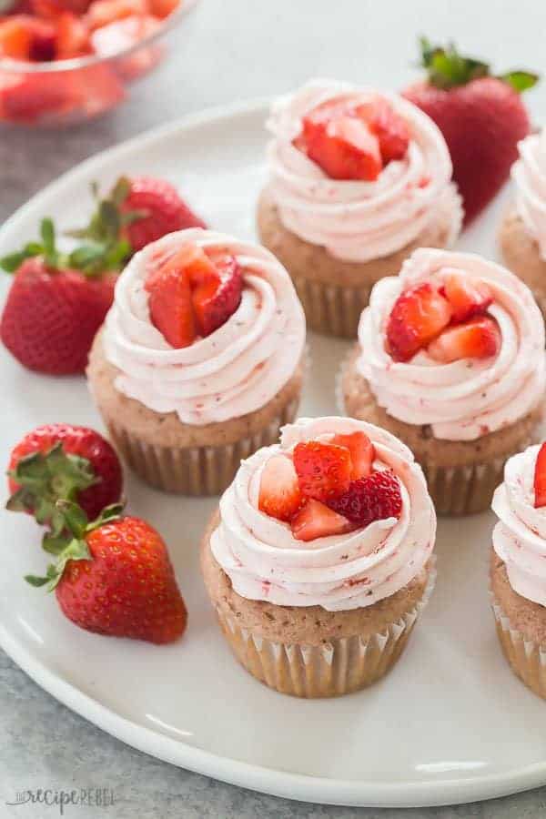 strawberry cupcakes with strawberry swiss meringue buttercream on a plate with fresh strawberries