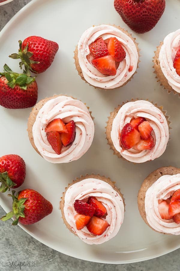 strawberry cupcakes with strawberry buttercream overhead on white plate with fresh strawberries on the side