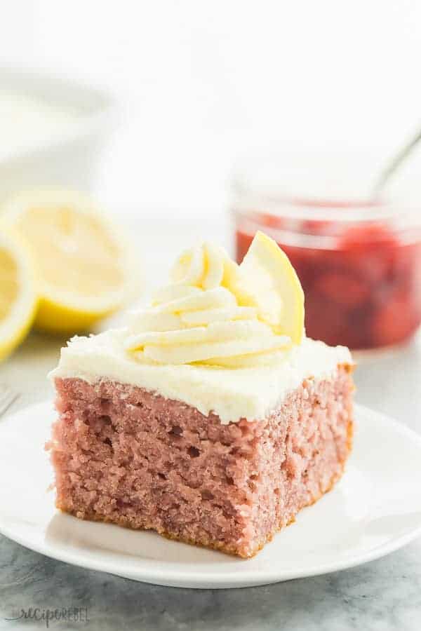 strawberry lemonade cake on white plate with lemon wedge and strawberry sauce in the background