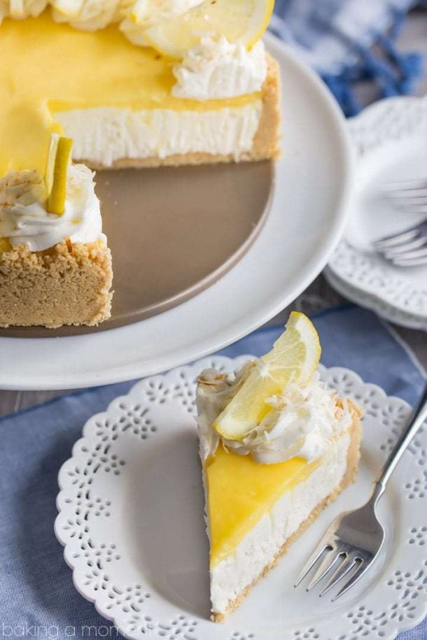 no bake lemon macaroon cheesecake slice on white plate with fork on plate and whipped cream and lemon slice on top