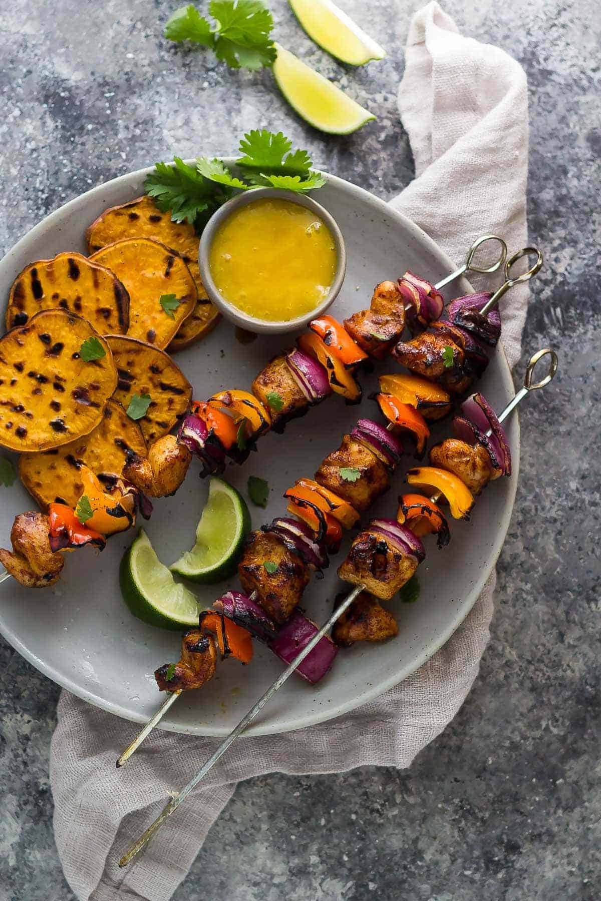 chili lime chicken kabobs with mango sauce on grey plate overhead on grey background