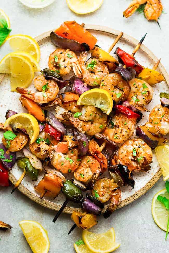 lemon shrimp skewers with peppers and red onions on white speckled plate with lemon wedges on the side
