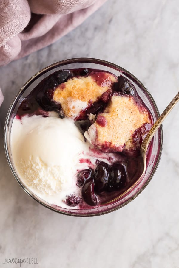 close up image of bowl of cherry cobbler with vanilla ice cream with spoon