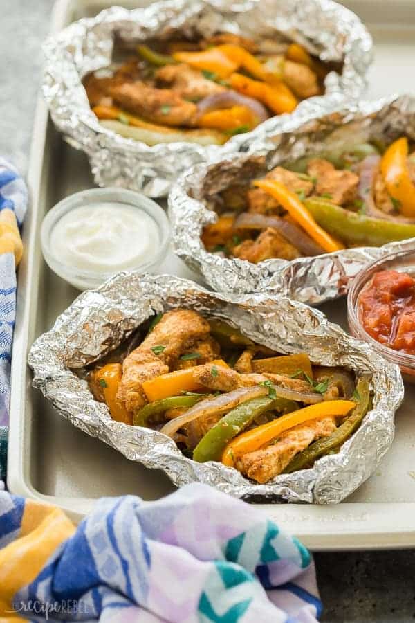 chicken fajita foil packets on sheet pan with small bowls of salsa and sour cream