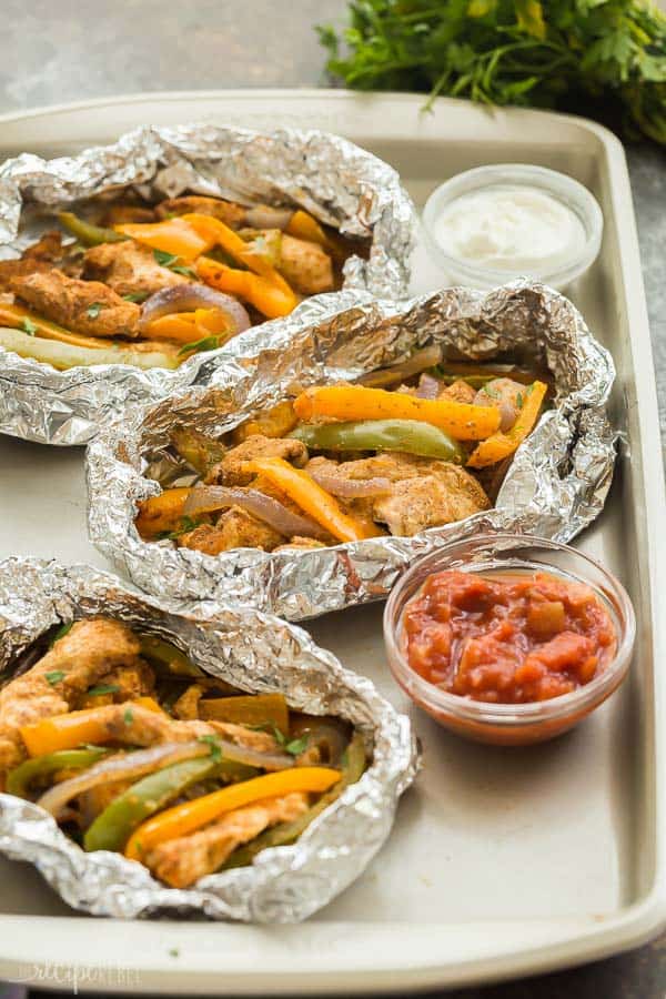 chicken fajita foil packs on sheet pan with salsa and sour cream and parsley in the background