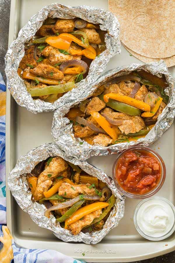 chicken fajita foil packets overhead on sheet pan with salsa and sour cream and tortillas