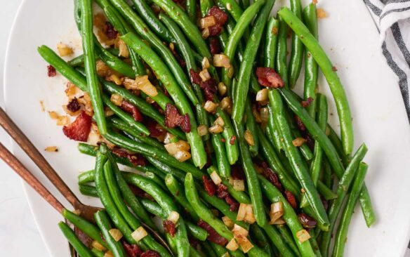 overhead image of green beans with bacon on white serving platter