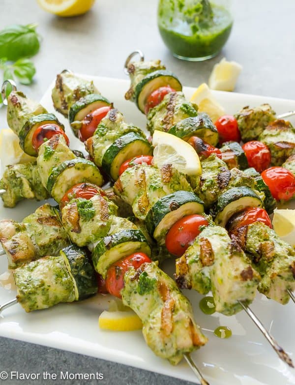 lemon pesto chicken kabobs on white plate with jar of pesto in the background