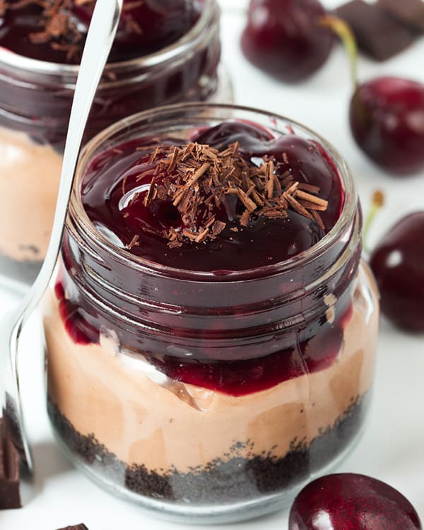 no bake chocolate cherry cheesecake jars with fresh cherries on the side and chocolate shavings on top