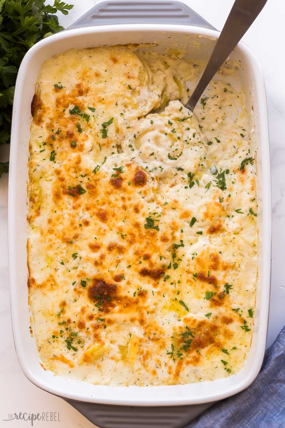 Overhead image of cheesy scalloped potatoes in white baking dish with spoon stuck in