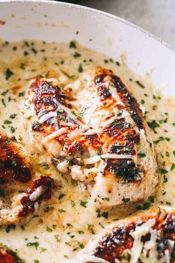 creamy garlic chicken in white skillet with lots of creamy sauce and sprinkled with fresh chopped herbs