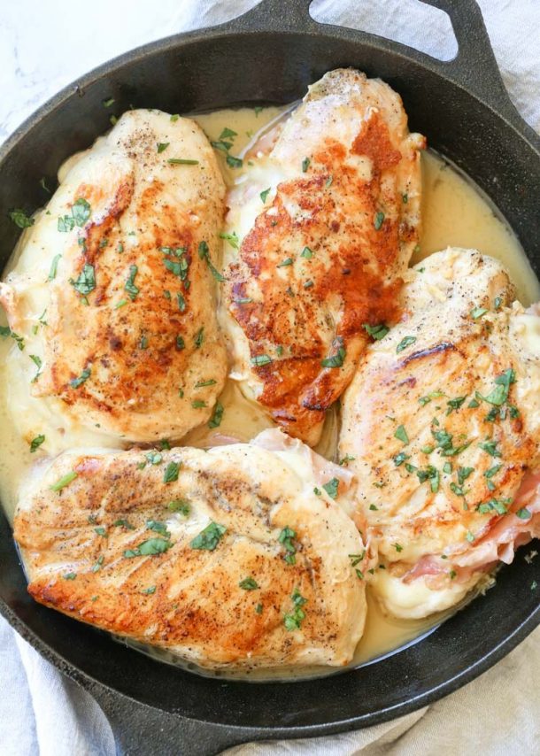 ham and cheese stuffed chicken breasts in a cast iron skillet with creamy sauce