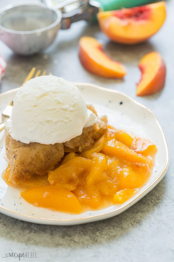 slow cooker peach cobbler with ice cream on white plate with fresh peaches in the background