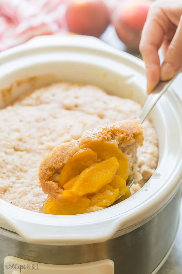scoop of slow cooker peach cobbler being pulled out of crockpot with metal spoon