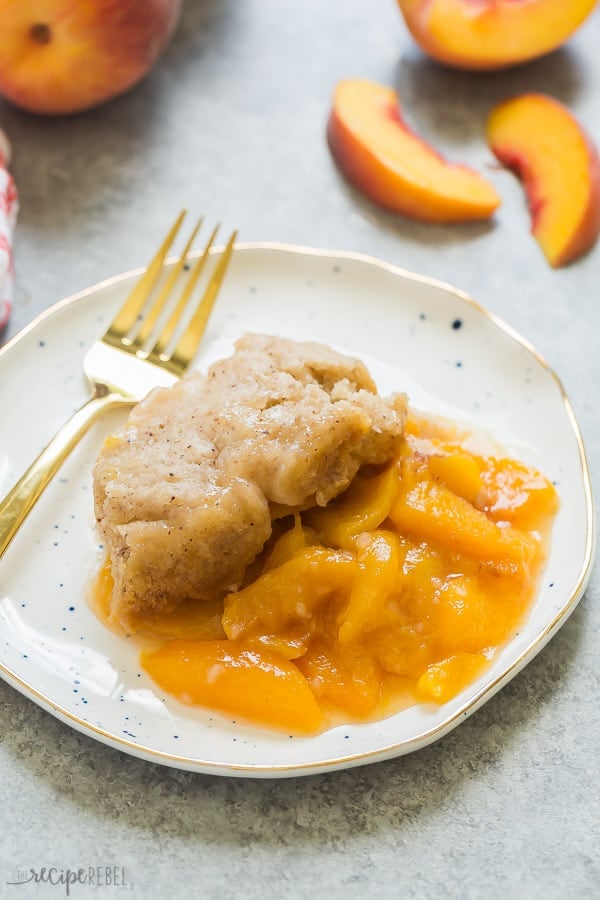 slow cooker peach cobbler on white plate with fresh peach slices in the background