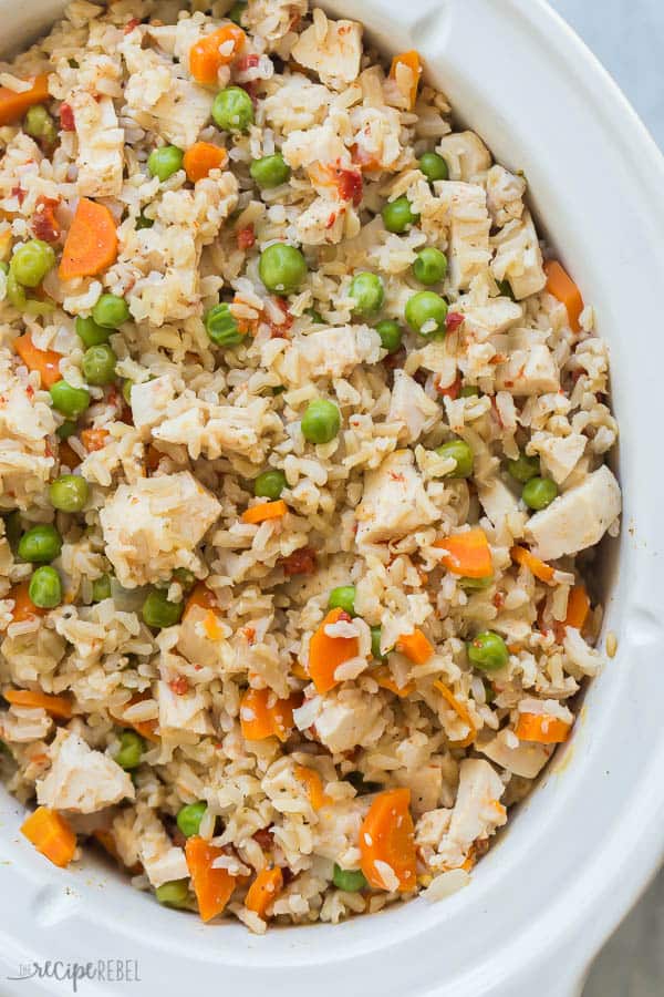 slow cooker chicken and rice overhead in white crockpot with chunks of chicken peas and carrots