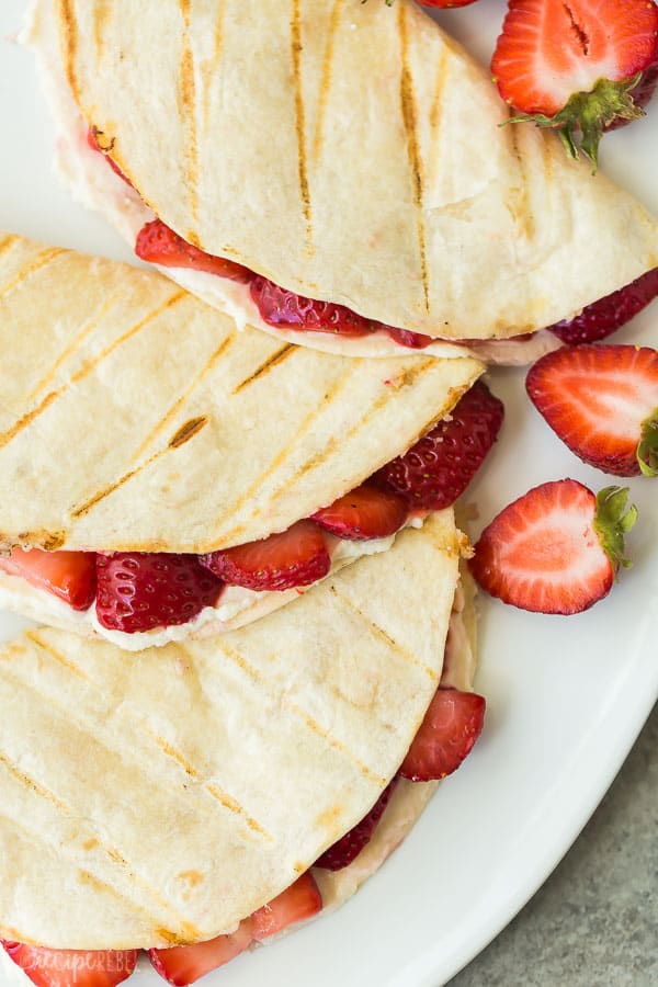strawberry cheesecake quesadillas overhead close up on white platter with fresh strawberry halves