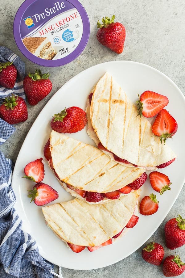 These Strawberry Cheesecake Quesadillas are a simple grilled dessert recipe that is easy to prepare and tastes incredible! Switch up the fruit and flavours to make your own variations, or take them to the stovetop to enjoy all year long. #cheesecake #strawberry #strawberries #quesadilla #dessert #recipe strawberry cream cheese quesadillas overhead on large white platter with fresh strawberries and strawberry halves all around