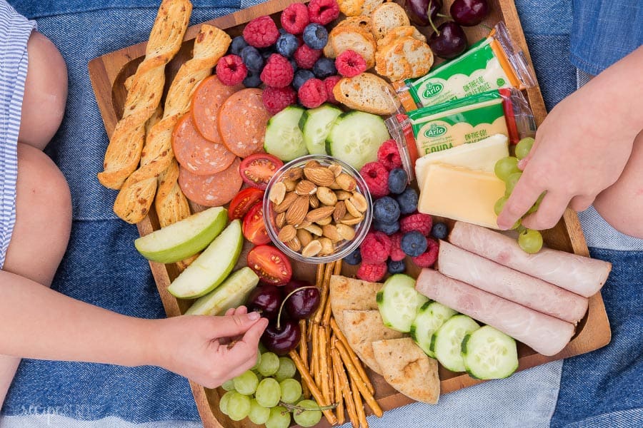 kids snack board on wooden board with two children reaching for snacks