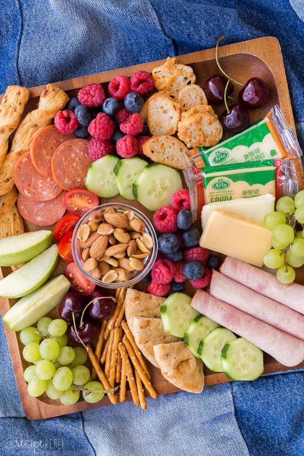 picnic foods to pack for a picnic as part of a covid outdoor date idea with apples, berries, nuts, pita, and meat on a charcuterie board