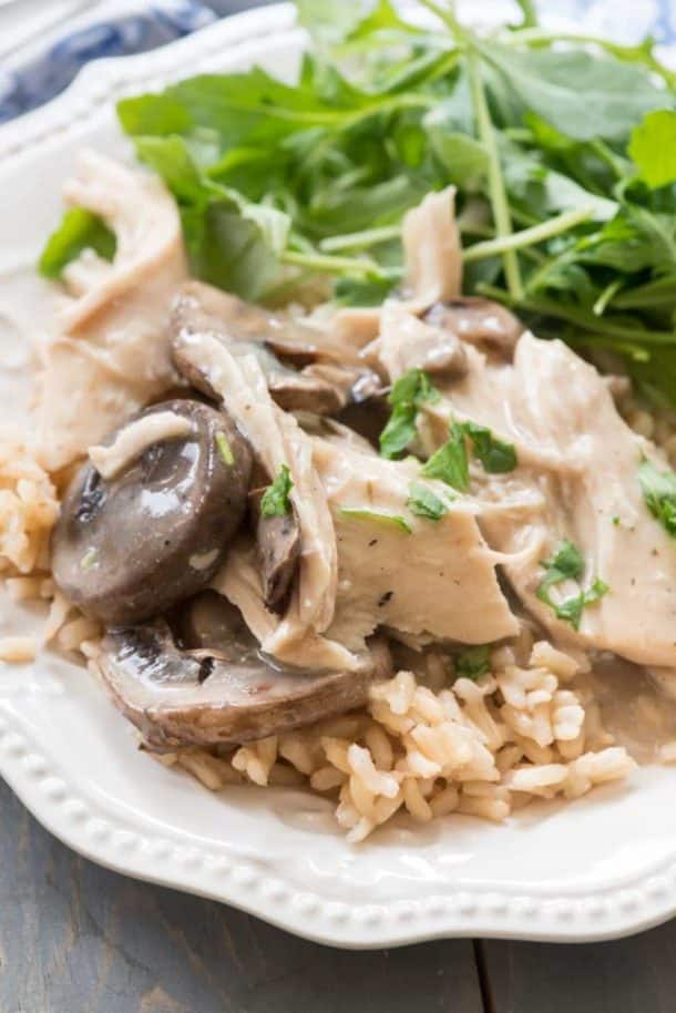crockpot mushroom chicken on a bed of rice on a white plate with fresh greens on the side