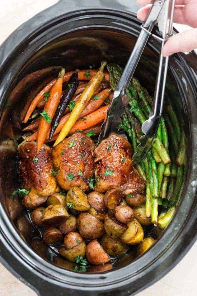 slow cooker harvest chicken with little potatoes asparagus and carrots in black crockpot