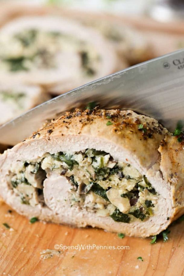 mushroom spinach stuffed pork tenderloin close up being sliced with large knife