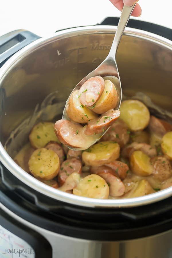 creamy sausage and potatoes in instant pot with a metal spoon scooping up some sausage and potatoes