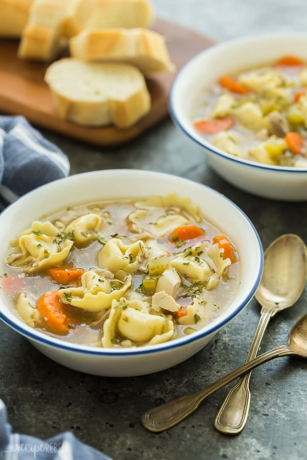 This Instant Pot Chicken Tortellini Soup is loaded with vegetables and cheese tortellini! The perfect chicken soup for a chilly day -- made in 30 minutes or less and freezer friendly! #soup #recipe #instantpot #pressurecooker #chicken #dinner instant pot chicken soup in white bowls with blue rim on dark grey background with bread in the background