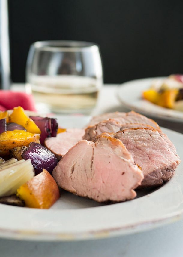 pork tenderloin recipes with peaches close up on white plate with glass of white wine in the background