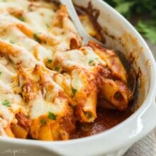 square image of ricotta stuffed shells being scooped out of baking dish.