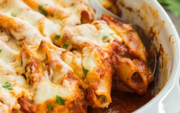 square image of ricotta stuffed shells being scooped out of baking dish.