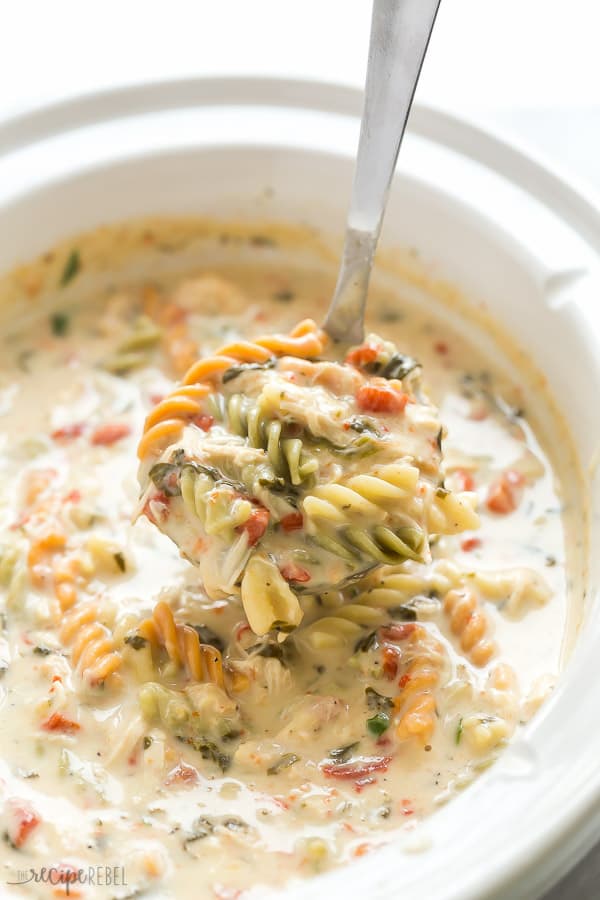 italian slow cooker chicken noodle soup in white crockpot with metal ladle scooping some soup