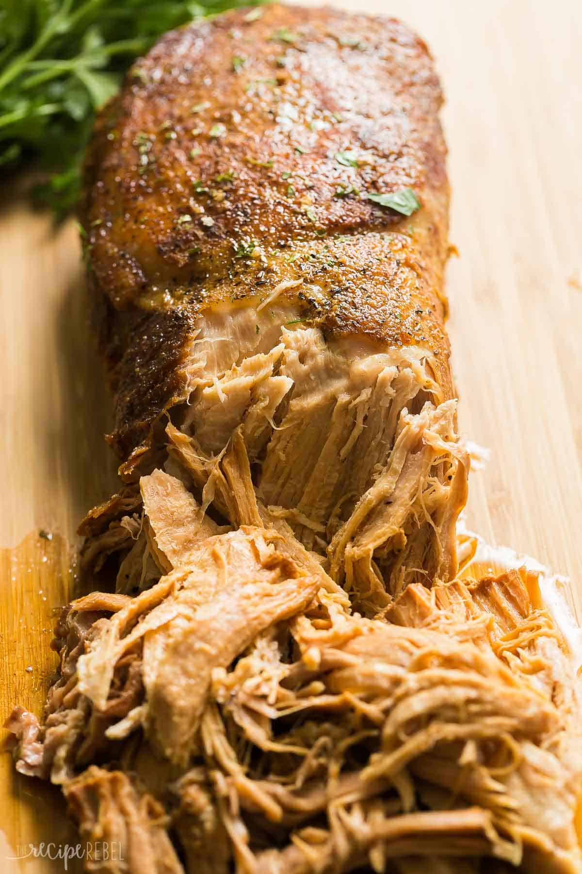 This easy Slow Cooker Pork Loin recipe includes a flavorful garlic herb rub, and is slow cooker in apple juice for extra flavor! It is fall apart tender with minimal effort! #slowcooker #crockpot #recipe #dinner #pork crockpot pork loin on a cutting board to shred.