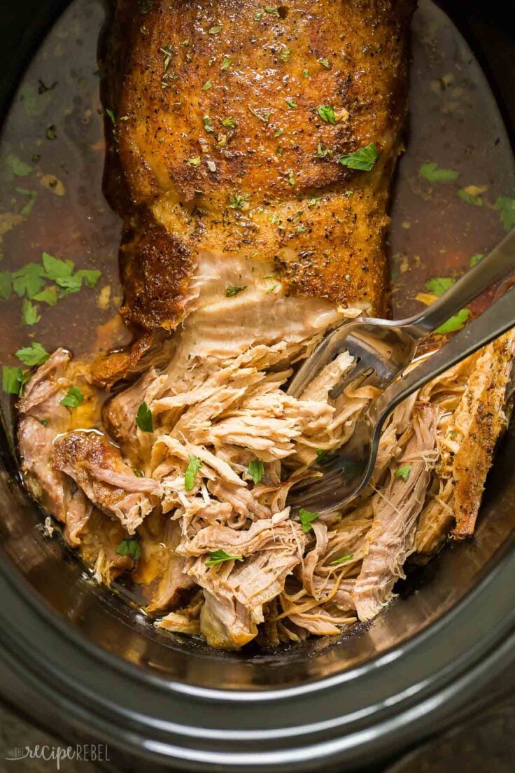 close up overhead image of crock pot pork loin with two forks shredding