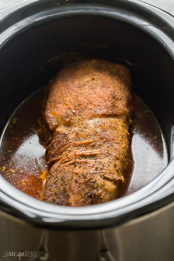 whole pork loin in slow cooker with seasoning and juices in the bottom of the crockpot