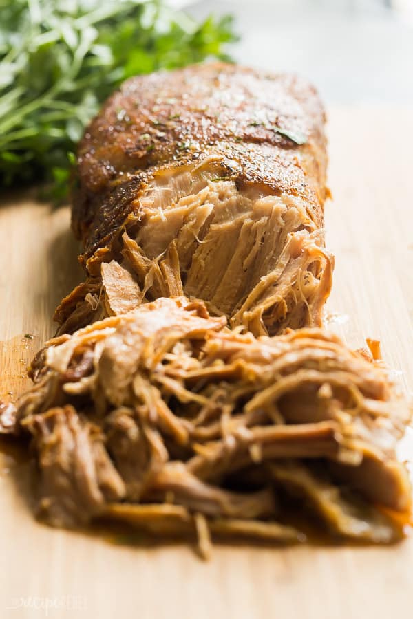 slow cooker pork loin shredded on wooden cutting board with fresh parsley in the background
