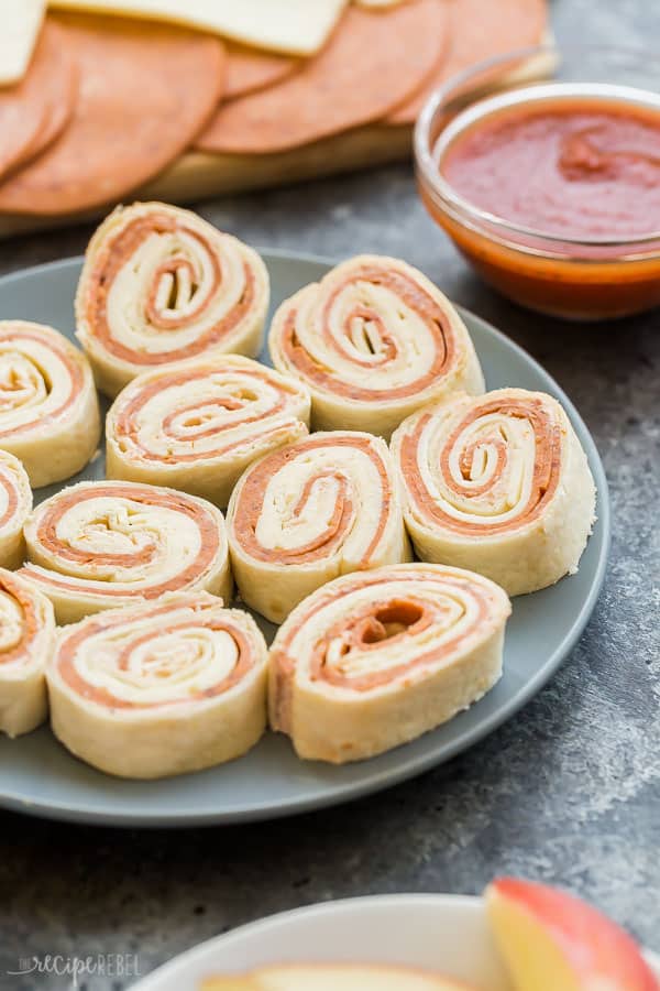 plate of tortilla roll ups up close up bowl of pizza sauce in the background