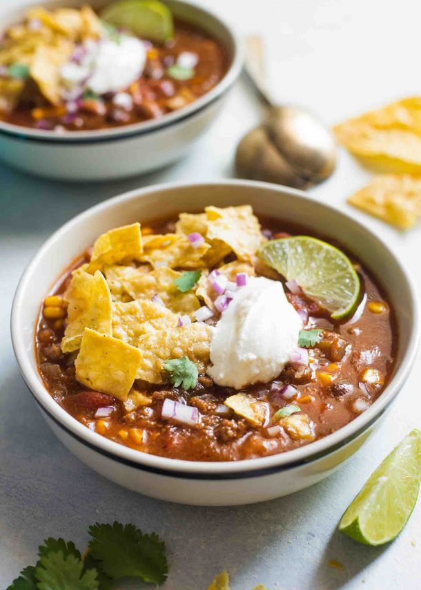 ground beef slow cooker taco soup two bowls topped with tortilla chips sour cream and lime slice