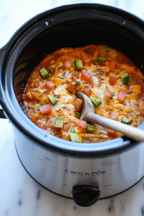 slow cooker ground beef enchilada stack in small black crockpot with wooden spoon stuck in