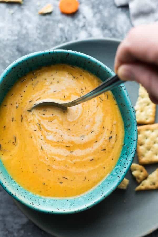 vegan carrot ginger soup in bright blue bowl with soda crackers on the side