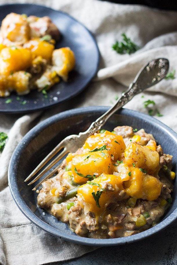 ground beef crock pot tater tot casserole on dark blue plates with fork stuck into casserole