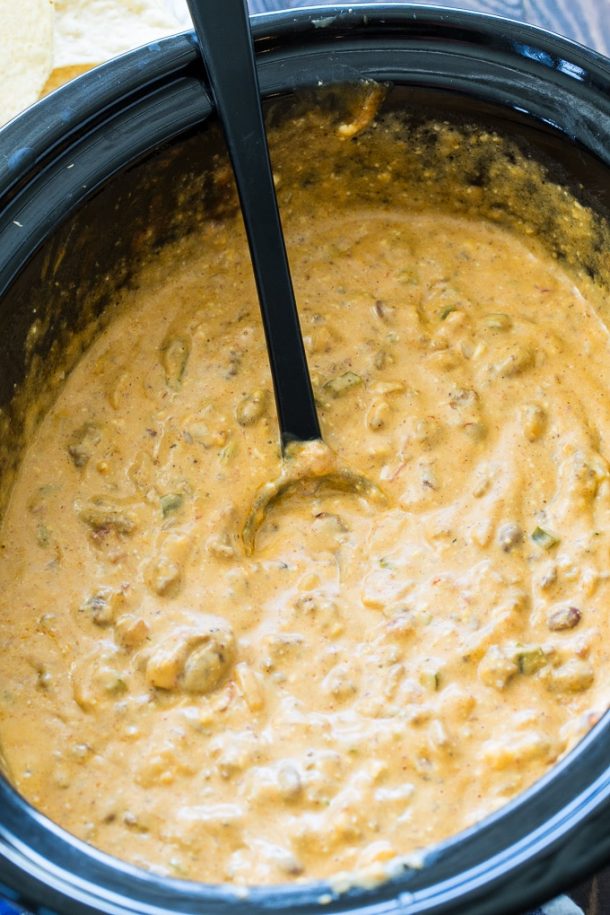 ground beef crock pot queso in black slow cooker with black serving spoon stuck in