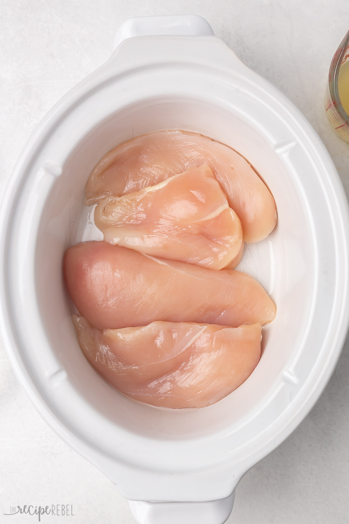 uncooked chicken breasts in white slow cooker.