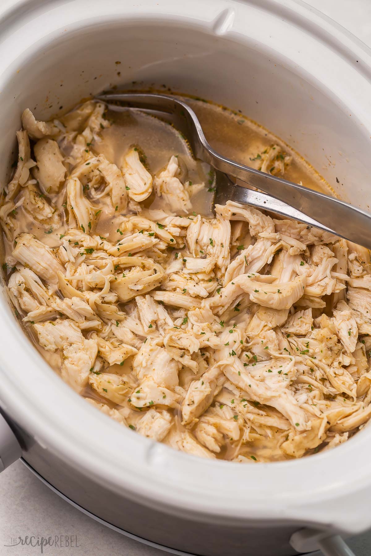 shredded chicken in juices in crockpot with two forks.