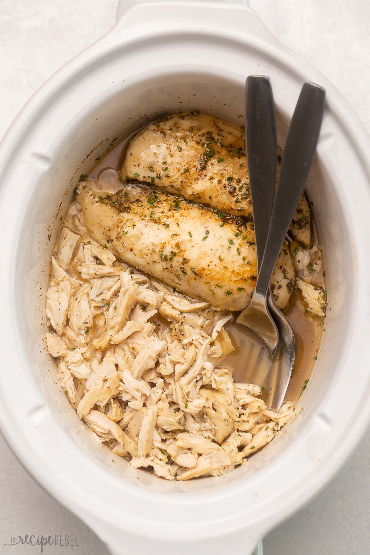 overhead image of two forks with shredded chicken and whole chicken breasts in crockpot.