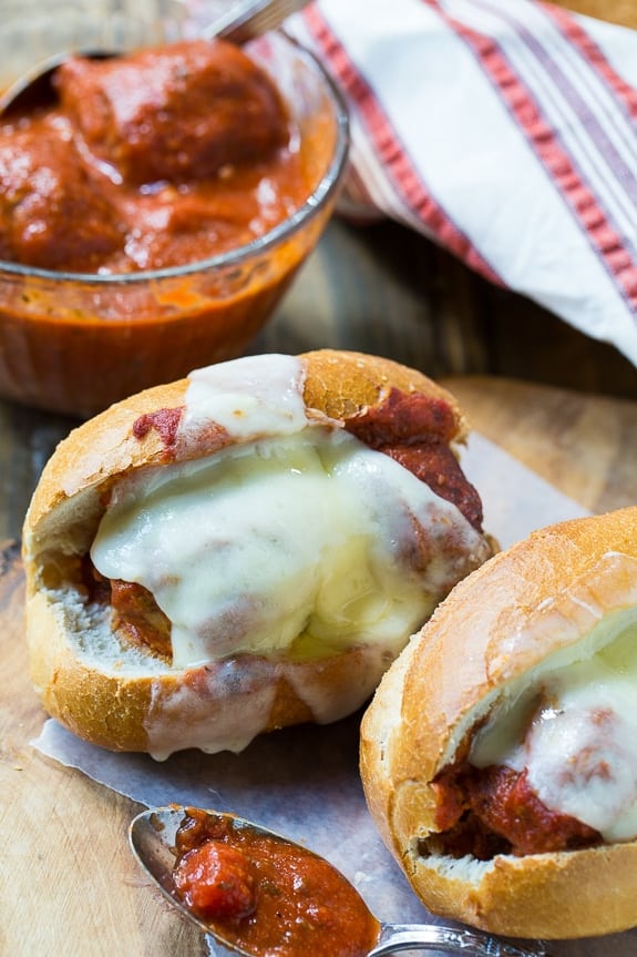 ground beef crock pot meatball subs on white buns with melted white cheese and meatballs in the background