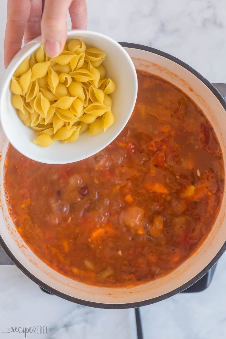 dry pasta being added to minestrone soup