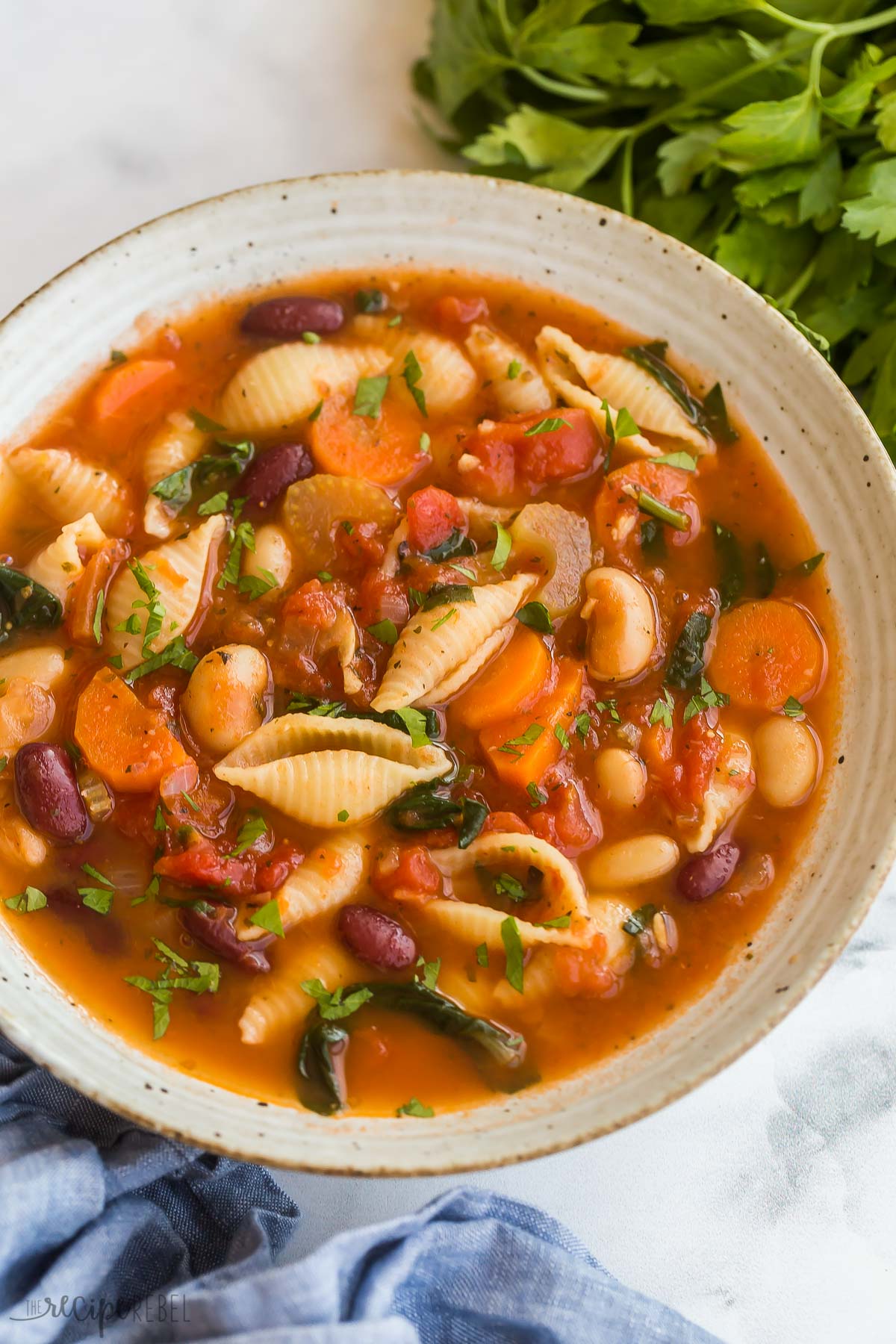 minestrone soup in beige bowl with blue towel and fresh parsley