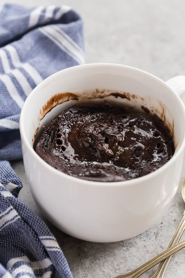 mocha chocolate mug cake in white mug on a grey background with blue striped towel in the background